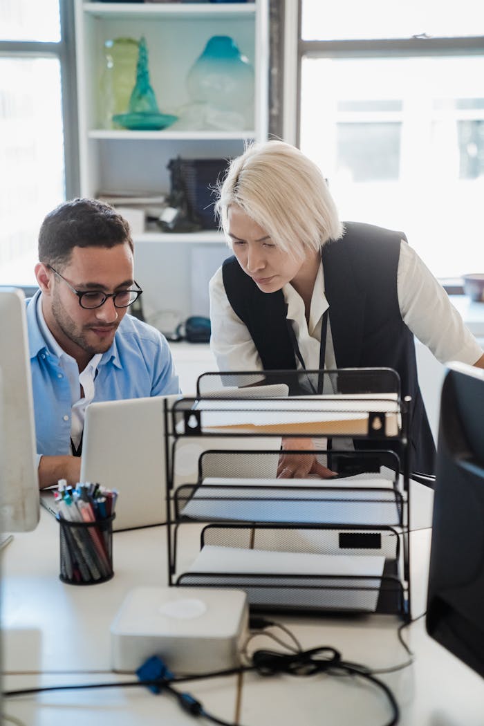 Two colleagues collaborate at a laptop in a bright, modern office environment, fostering teamwork and productivity.
