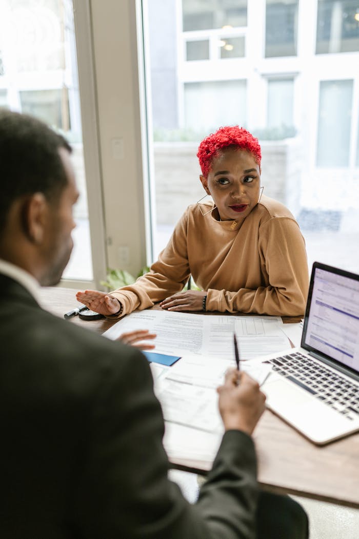 Two colleagues in a business meeting discussing documents in an office setting.